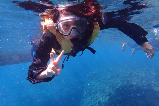 沖縄の海でシュノーケリングを楽しむ女性が、水中でピースサインをしている様子